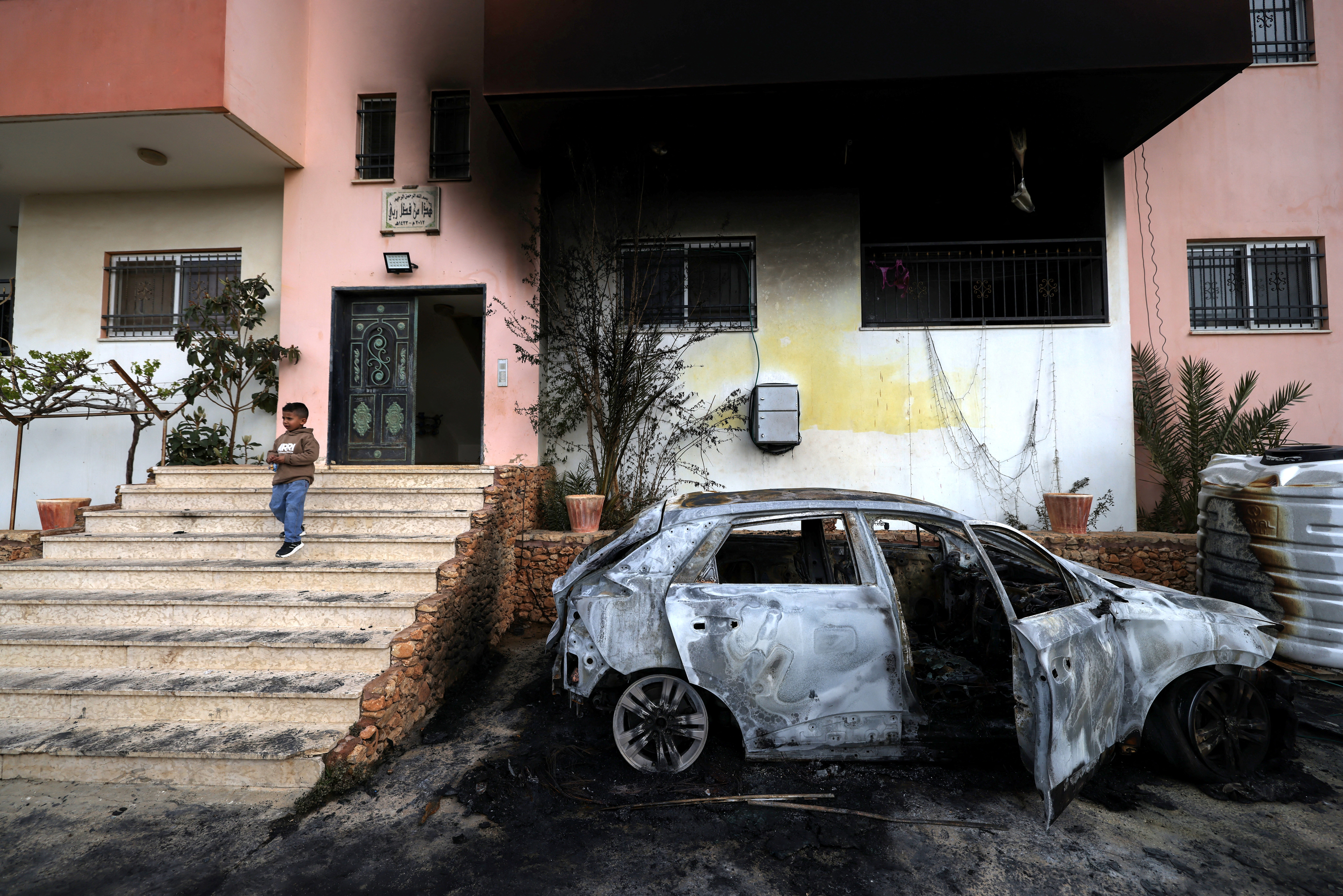TOPSHOT - A Palestinian child stands outside a destroyed car and burnt out home following a reported attack by Israeli settlers in the village of Deir al-Hatab, east of the city of Nablus, in the Israeli-occupied West Bank on March 23, 2026. Palestinian residents said on March 22, 2026, that Israeli settlers torched buildings and cars in attacks on several villages in the occupied West Bank, with Israel's army condemning "violence of any kind" after the fact.  Violence in the Palestinian West Bank, which Israel has occupied since 1967, has soared since the Hamas attack on Israel triggered the Gaza war in October 2023. (Photo by JAAFAR ASHTIYEH / AFP via Getty Images)