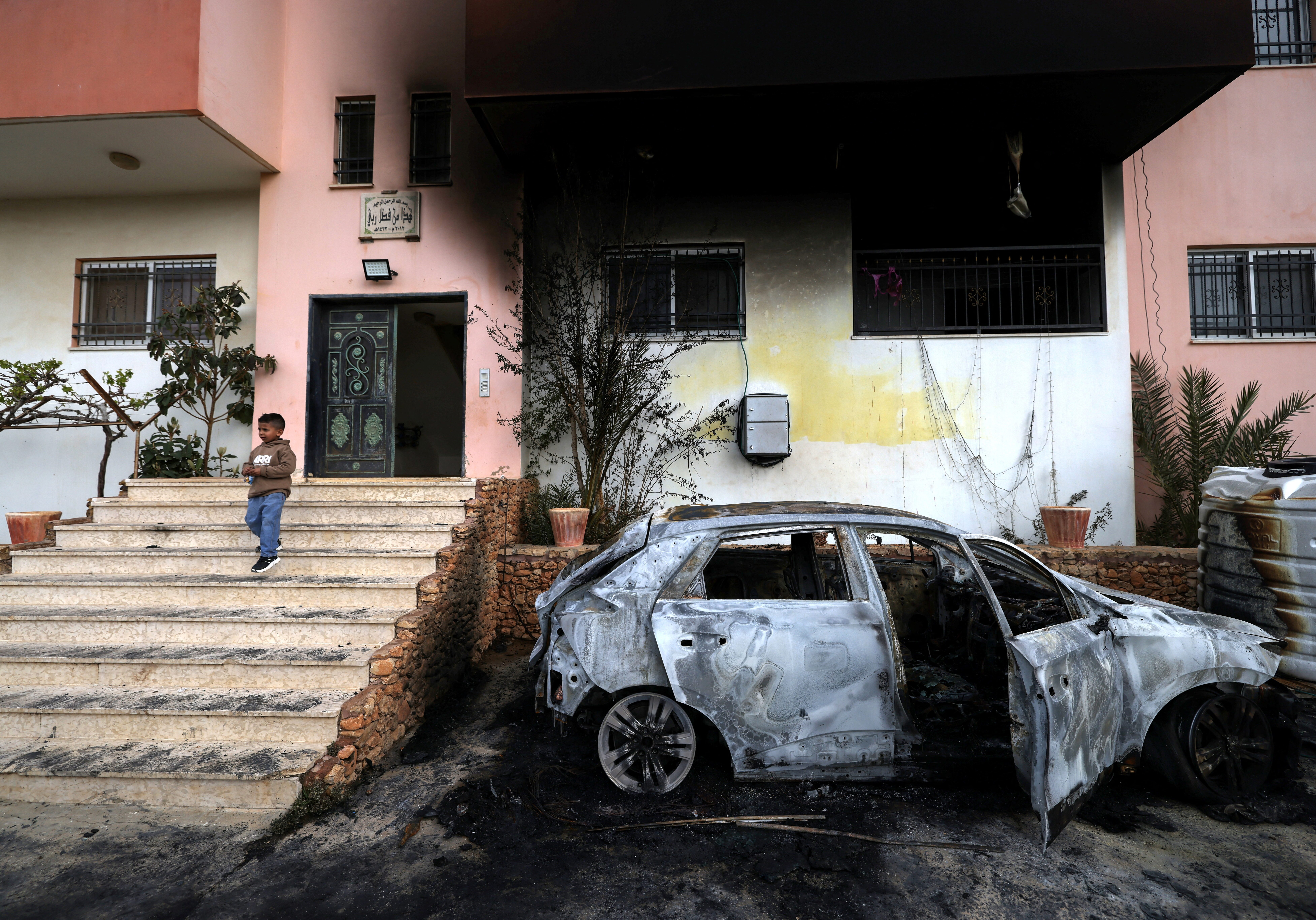 TOPSHOT - A Palestinian child stands outside a destroyed car and burnt out home following a reported attack by Israeli settlers in the village of Deir al-Hatab, east of the city of Nablus, in the Israeli-occupied West Bank on March 23, 2026. Palestinian residents said on March 22, 2026, that Israeli settlers torched buildings and cars in attacks on several villages in the occupied West Bank, with Israel's army condemning "violence of any kind" after the fact.  Violence in the Palestinian West Bank, which Israel has occupied since 1967, has soared since the Hamas attack on Israel triggered the Gaza war in October 2023. (Photo by JAAFAR ASHTIYEH / AFP via Getty Images)